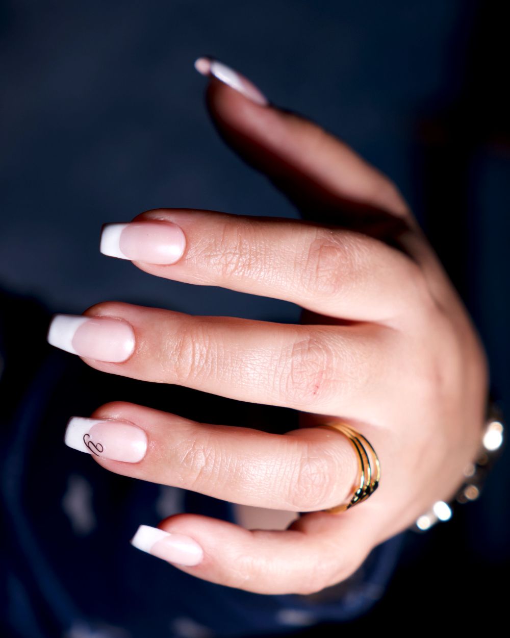 Licensed stock photograph: a hand with a fresh French manicure, square white tips, resting against a dark background.