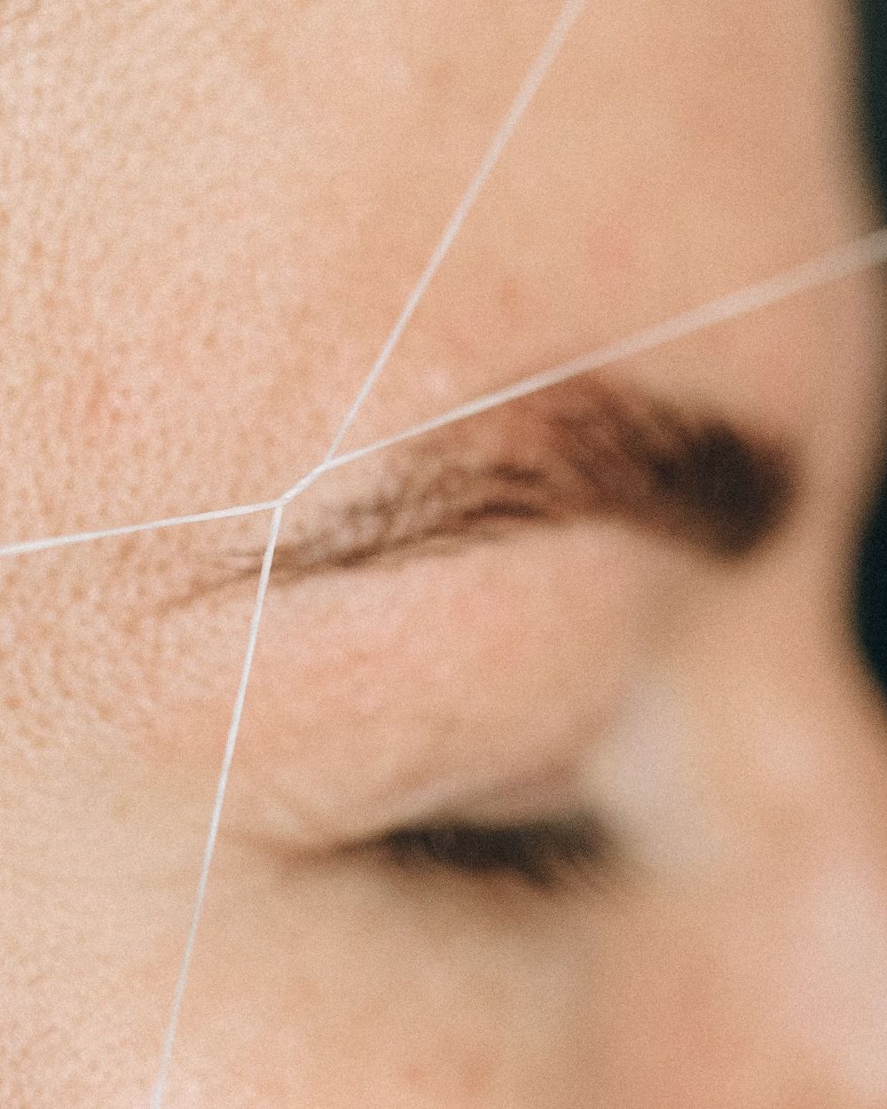 Licensed stock photograph: a cotton thread drawn taut across a brow line during eyebrow threading, shown as a close detail.
